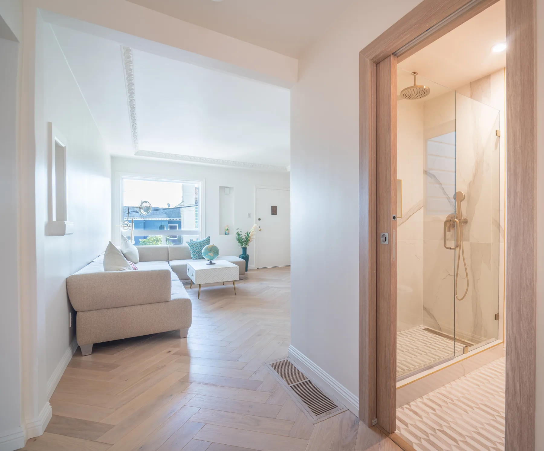 Open-plan living space with herringbone floors and renovated bathroom by Lussoro Design + Build