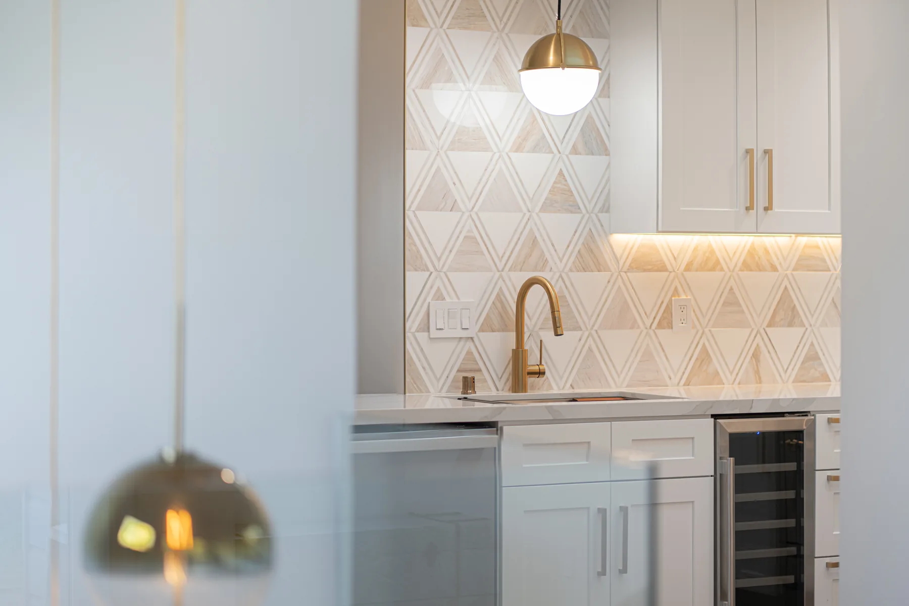 Kitchen sink area with white cabinetry, brass faucet and geometric backsplash by Lussoro Design + Build